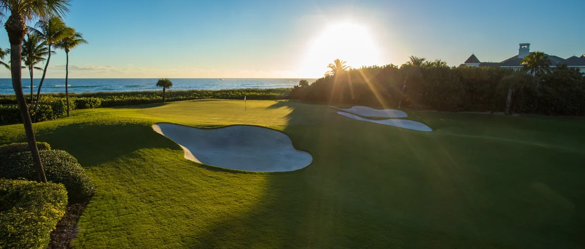 Golden light across the oceanfront 18th hole at Sailfish Point as waves meet the shoreline