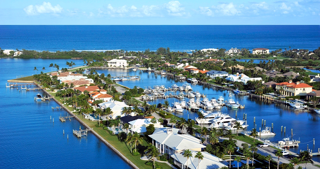 Aerial view of a marina with boats, docks, canals, waterfront homes, and the ocean beyond.