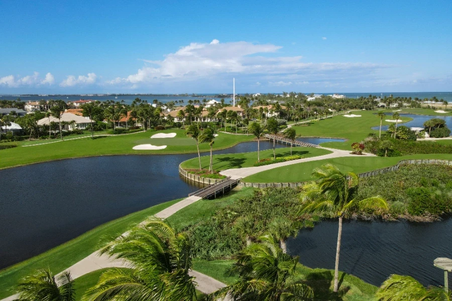 Aerial view of coastal golf course with greens, water features, and palm trees
