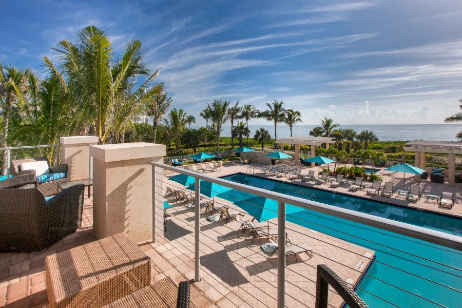 Oceanfront pool terrace with lounge chairs, umbrellas, and palm trees overlooking the water