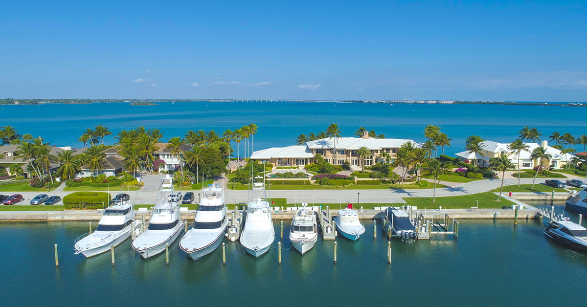 Boats docked at marina in front of waterfront homes and ocean.