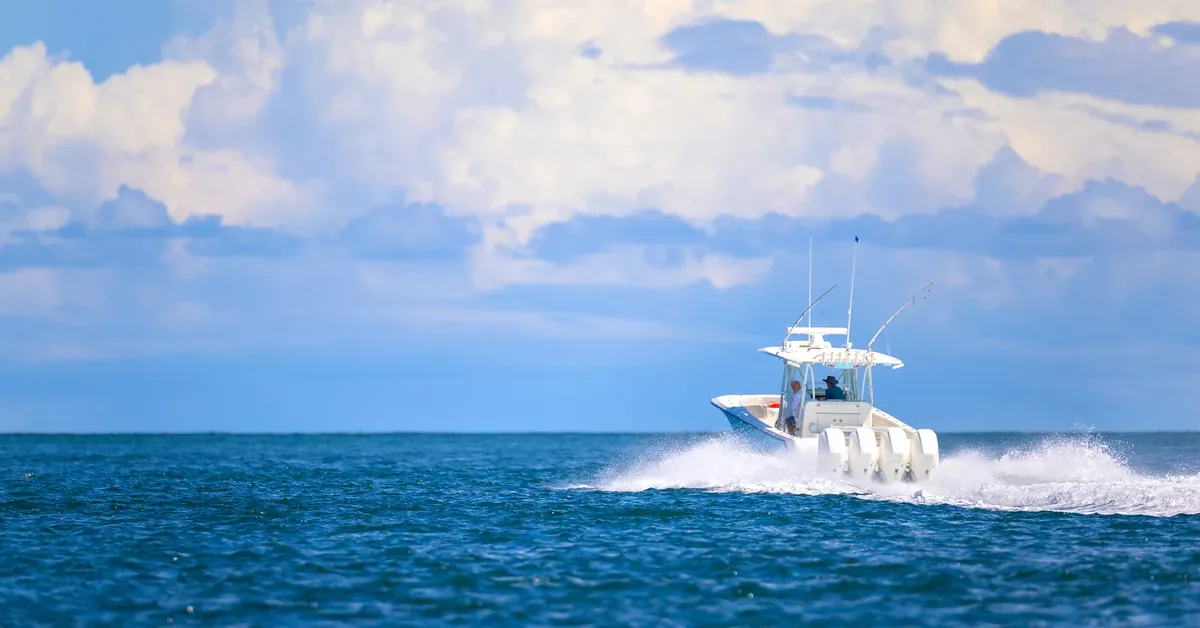 A white sport fishing boat speeds across deep blue open waters beneath dramatic cumulus clouds on a sunny day.