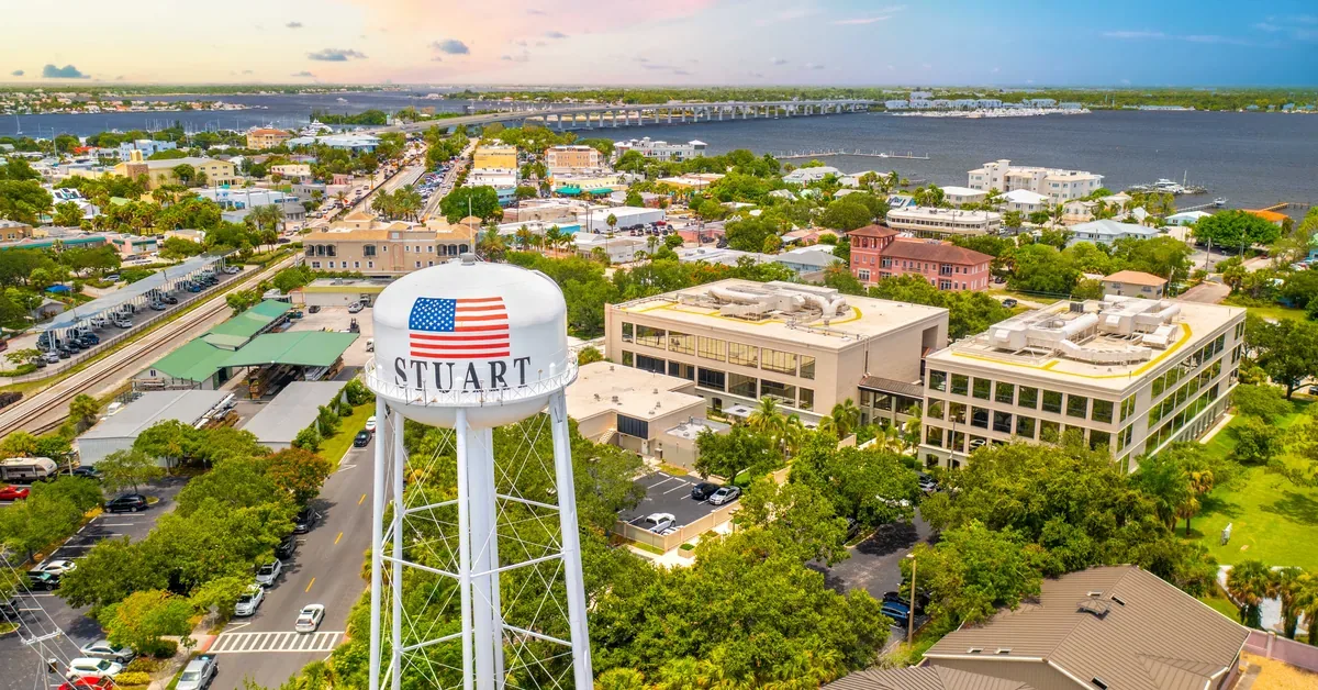 Aerial view of Stuart, Florida's charming waterfront downtown, featuring the iconic water tower with American flag against a pastel sunset sky.